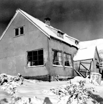 Close up view of Albury Ski Club Lodge surrounded by snow. 2 people are standing in front of the doorway. Icicles hanging from eaves.