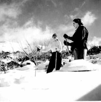 Two women on skis surrounded by snow. Ominous clouds overhead