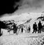 A large group of skiers gathered outside a building at the foot of a slope.