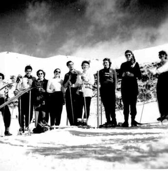 Group of nine skiers with skis and poles. Ominous clouds overhead.