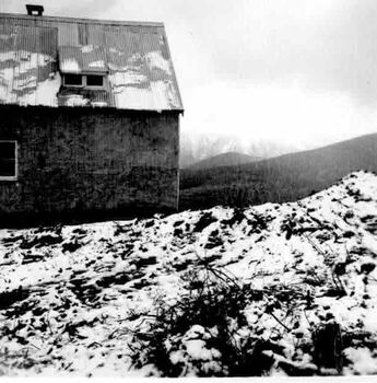 Building with corrugated iron roof on left. Thinly snow covered mountain in background