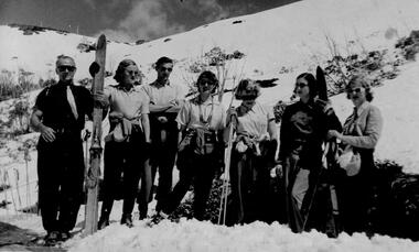 A group of skiers holding skis and poles. Snow covered slope in background