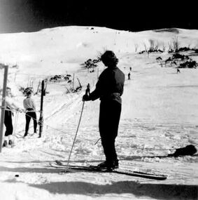 A woman standing at the top of tow with other skiers in front of her and going up the slope.