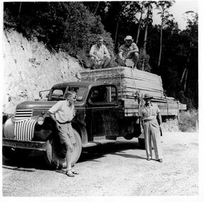 Four men and a truck loaded with timber.framework. Two of the men are on top of the load attaching ropes.