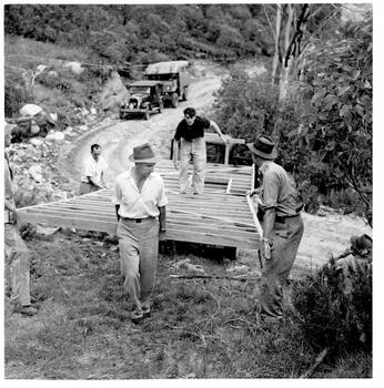 Men unloading timber frames from truck. Other vehicles in the background.