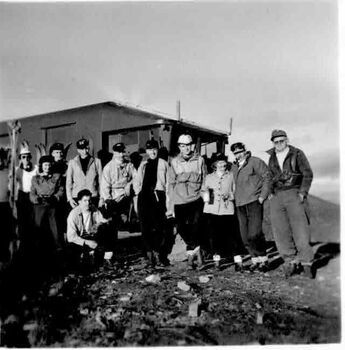 Group assembled in front of hut. No snow on ground.