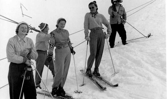 Three women on skis and two men who are holding skis over their shoulders.