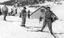 Skiers near the tow visible in background. Man on tow in foreground has long trousers and a sleeveless shirt.