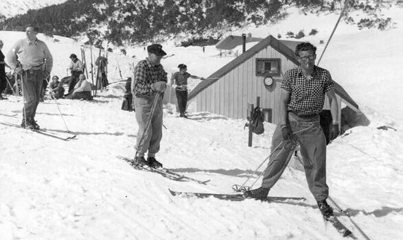 Skiers near the tow visible in background. Man on tow in foreground has long trousers and a sleeveless shirt.