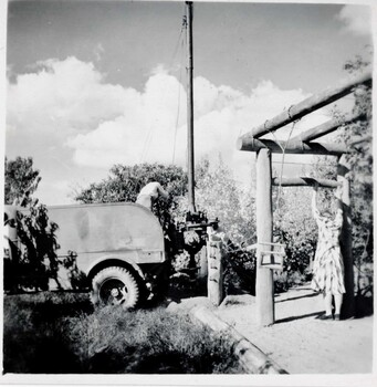 Putting up light pole near lodge. Man operating machinery while woman watches at right.