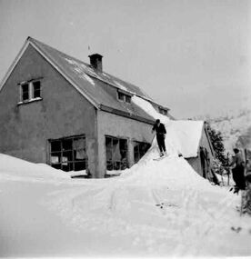 A man using the verandah roof of the lodge as a ski jump.
