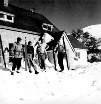 Five  people with skis in front of lodge in heavy snow