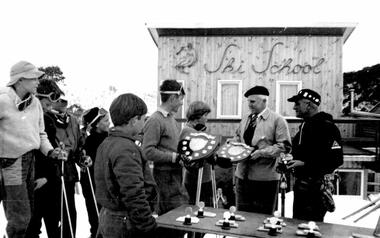 Boys being presented with shield trophies. Falls Creek Ski School building in background