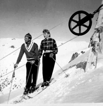 Two skiers standing on the slope beside a wheel of the ski lift
