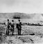 Three men with their backs to the camera looking towards smoke in the distance. Three other men are near a line of fallen timber 