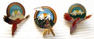Three enamelled badge featuring mountains, rainbow and birds.