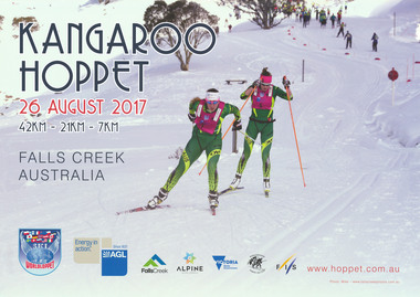 Two Australian skiers on a downhill slope with a group of spectators in the background.
