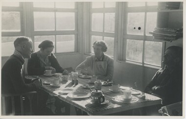 Four people sitting at table in front of large windows.