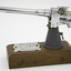 Rectangle wooden base with model gun mounted on one end with silver engraved label screwed on top of base next to base of gun model.