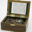 Rectangular honey coloured wooden box with hinged lid, open, shows printed paper history about the item in lid and metal torch in box.