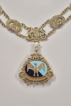 Close up of medallion of the Borough of Eaglehawk mayoral chain. Triangular shape depicting an eagle with outspread wings in gold on a light and dark blue enamel background. Dated 1862.