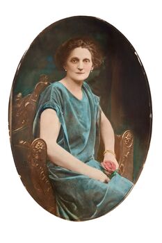  Oval shaped three quarter studio portrait depicting a seated woman in a green evening dress holding a rose. 