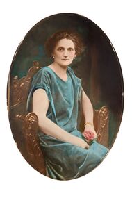  Oval shaped three quarter studio portrait depicting a seated woman in a green evening dress holding a rose. 