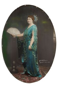 Oval shaped full length studio portrait depicting a standing  woman in a green evening dress holding an open fan in her right hand. 	