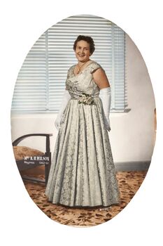 Oval shaped studio portrait depicting a standing woman in a white evening dress wearing white gloves and the Mayoress medallion. 