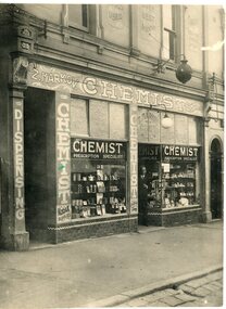 Black and white image of a Chemist Shop with a man in the doorway. 