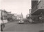 A busy city street with vintage cars and buildings. A truck loaded with timber is on the left side of the street.