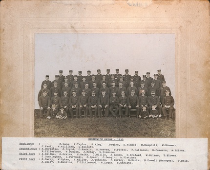 A group of men in uniform are seated on benches outdoors, with grass to the right with a typed list attached,