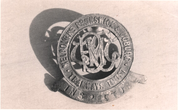 A circular metallic badge with ornate letters MBCTT in the center, surrounded by the text "MELBOURNE BRUNSWICK & COBURG TRAMWAY TRUST INSPECTOR" in a circular pattern.