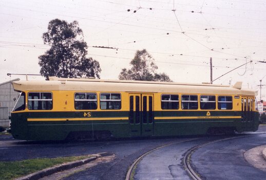 A yellow and green tram with multiple windows and double doors is positioned on tram tracks.