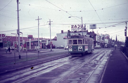 A vintage green and cream tram numbered 801 travels along wet tram tracks on a city street lined with buildings and businesses.