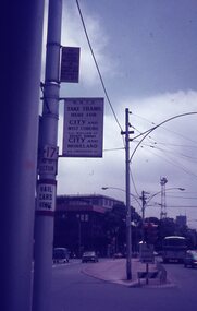 Street scene with tram signs indicating routes to the city, West Coburg, and Moreland, with cars and buildings visible.