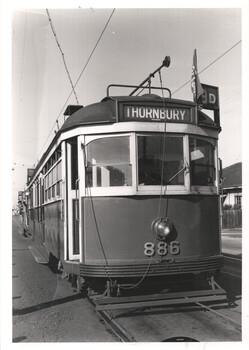 Low-angle shot of a vintage tram numbered 886. The tram has a sign above the windshield that reads "THORNBURY" and a destination sign indicating "9D". The tram is on tracks with overhead power lines.