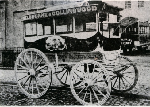 Horse-drawn omnibus labeled "MELBOURNE & COLLINGWOOD" with ornate decoration on its side, parked on a cobbled street.