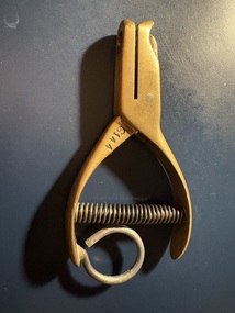 A brass single-hole punch with a spring mechanism and a looped handle, marked with "G144".