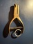 A brass single-hole punch with a spring mechanism and a looped handle.