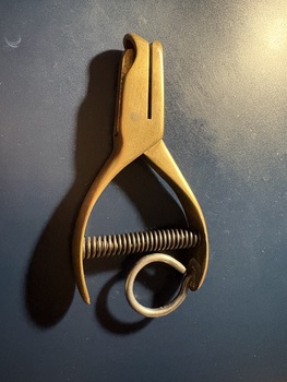 A brass single-hole punch with a spring mechanism and a looped handle.