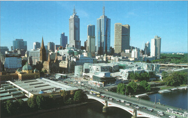 Panoramic view of a cityscape featuring a river in the foreground with a bridge, and a dense collection of modern skyscrapers and historical buildings in the background under a clear blue sky.