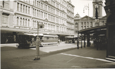 Street scene with multiple cable cars and pedestrians in front of ornate, multi-story buildings.