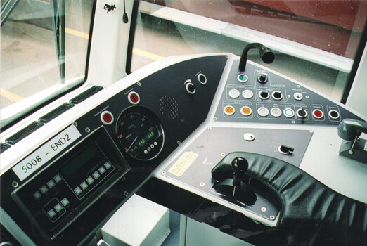 Close-up view of a tram driver's cabin dashboard, showing controls, a speedometer, a digital display, and a throttle lever covered by a leather gaiter.