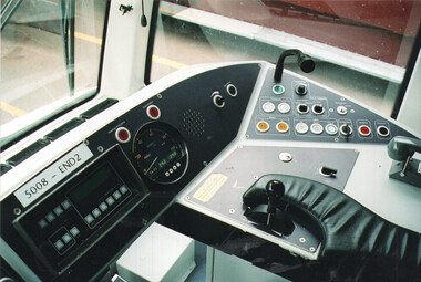 Close-up view of a tram driver's cabin dashboard, showing controls, a speedometer, a digital display, and a throttle lever covered by a leather gaiter.