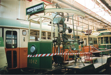 A vintage tram, marked with "1042", is on display in a workshop setting with other trams visible in the background.