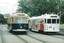 Two historic trams on tram tracks; one is dark green and cream with "BRIGHTON BCH" on the front and number 53, the other is white with colorful abstract art and "CITY CIRCLE" on the front with number 909.