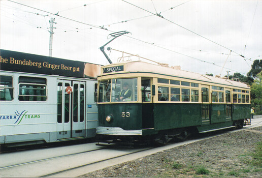 A vintage green and cream tram numbered 53, labeled "SPECIAL" on top, stands on tram tracks beside a modern silver tram with "YARRA TRAMS" branding and a "Bundaberg Ginger Beer" advertisement.