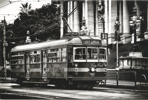 A vintage "City Circle" tram with the number 981 displayed, stopped on a city street in front of ornate classical architecture.