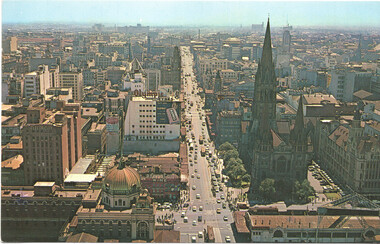 Aerial view of a bustling city street lined with tall buildings, including a prominent church with a spire, and a long line of traffic moving down Swanston St from the south.
